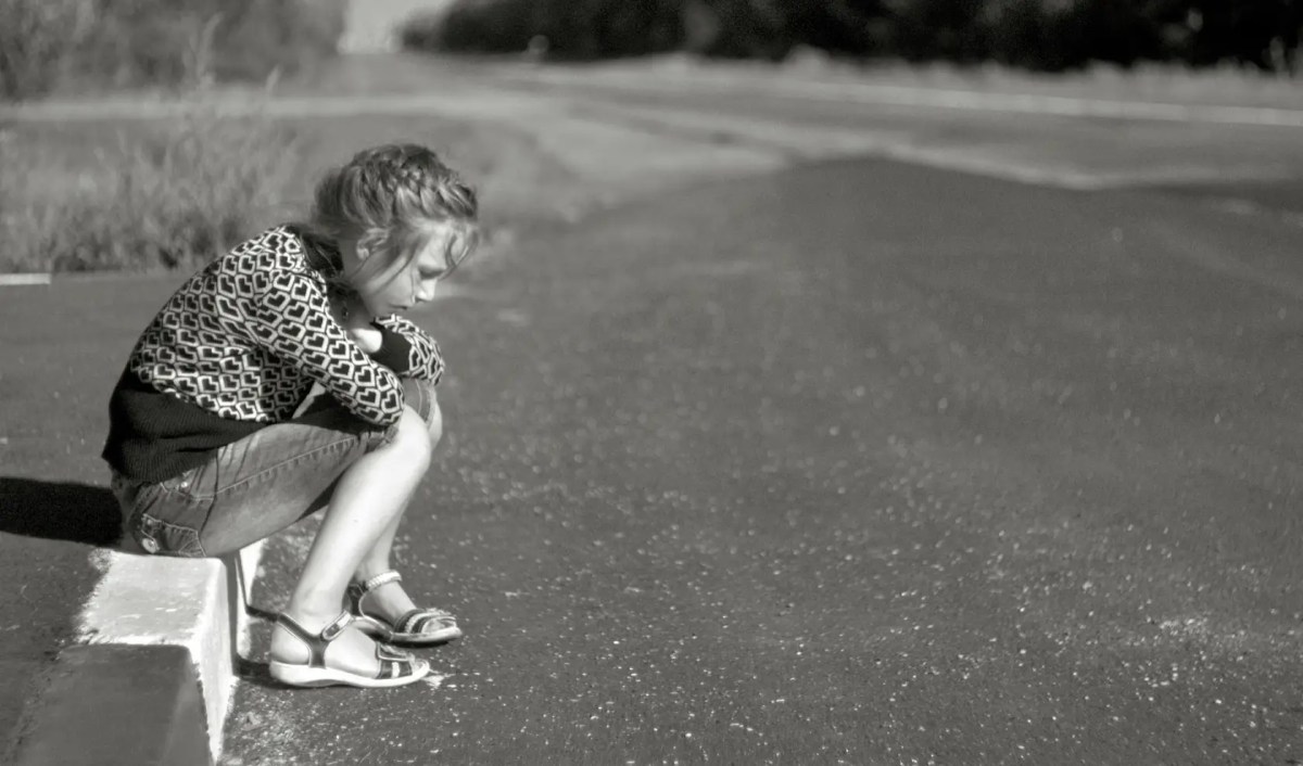 Seorang wanita yang terlihat sedih sedang duduk sendirian di pinggir jalan